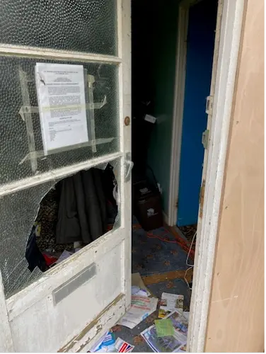 A door with a broken glass panel and scattered items on the floor.
