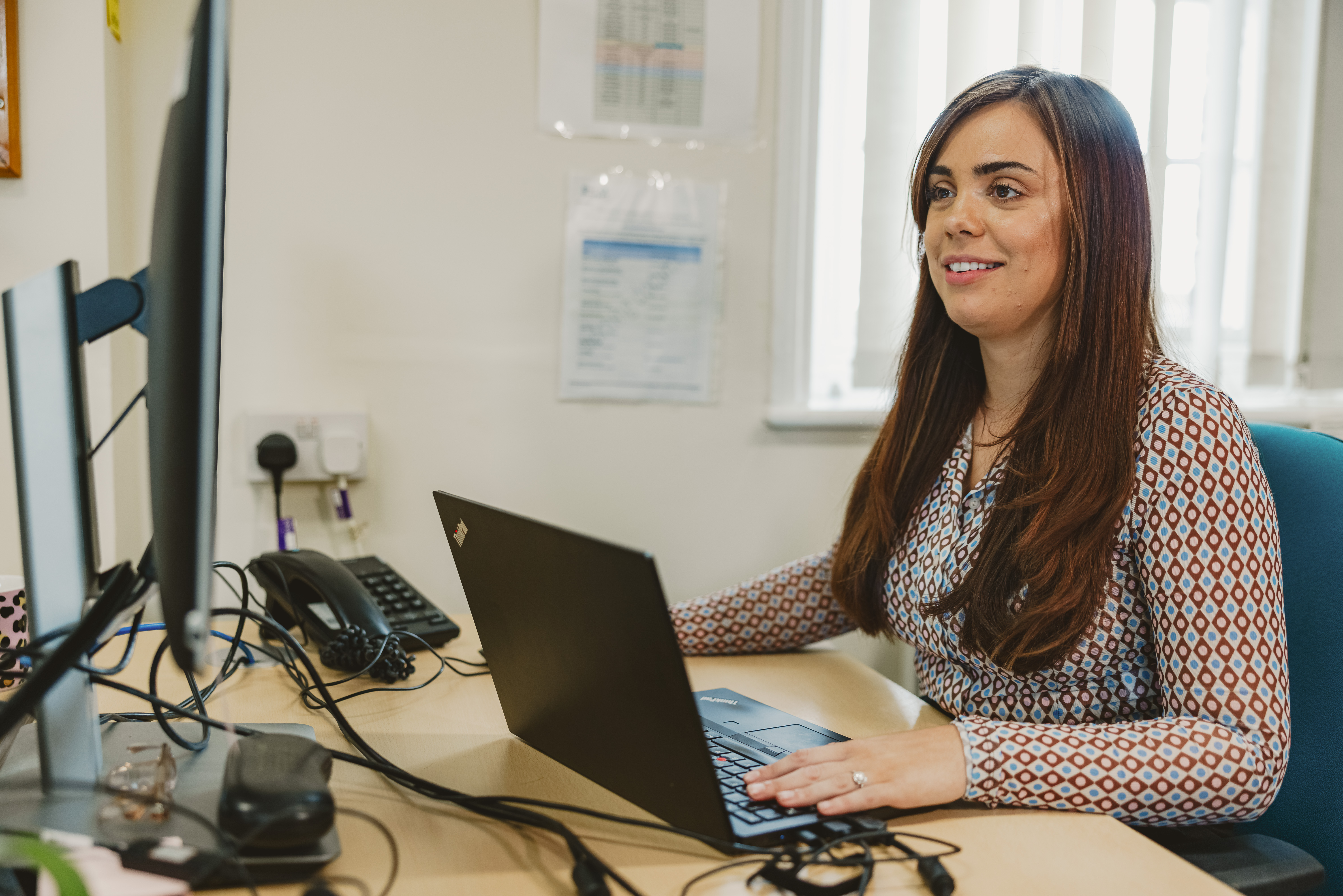 Woman with long brown hair, working at the desk.